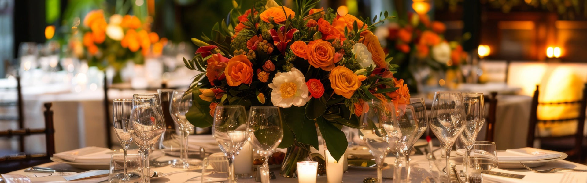 Elegant corporate event floral centerpiece with orange roses and anemones on a candlelit banquet table.