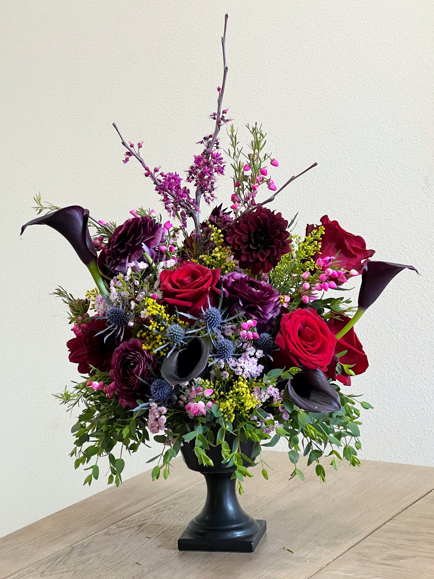 dark and moody urn floral arrangement with dahlias, ranunculus, calla lilies, blue thistle, and gypsum