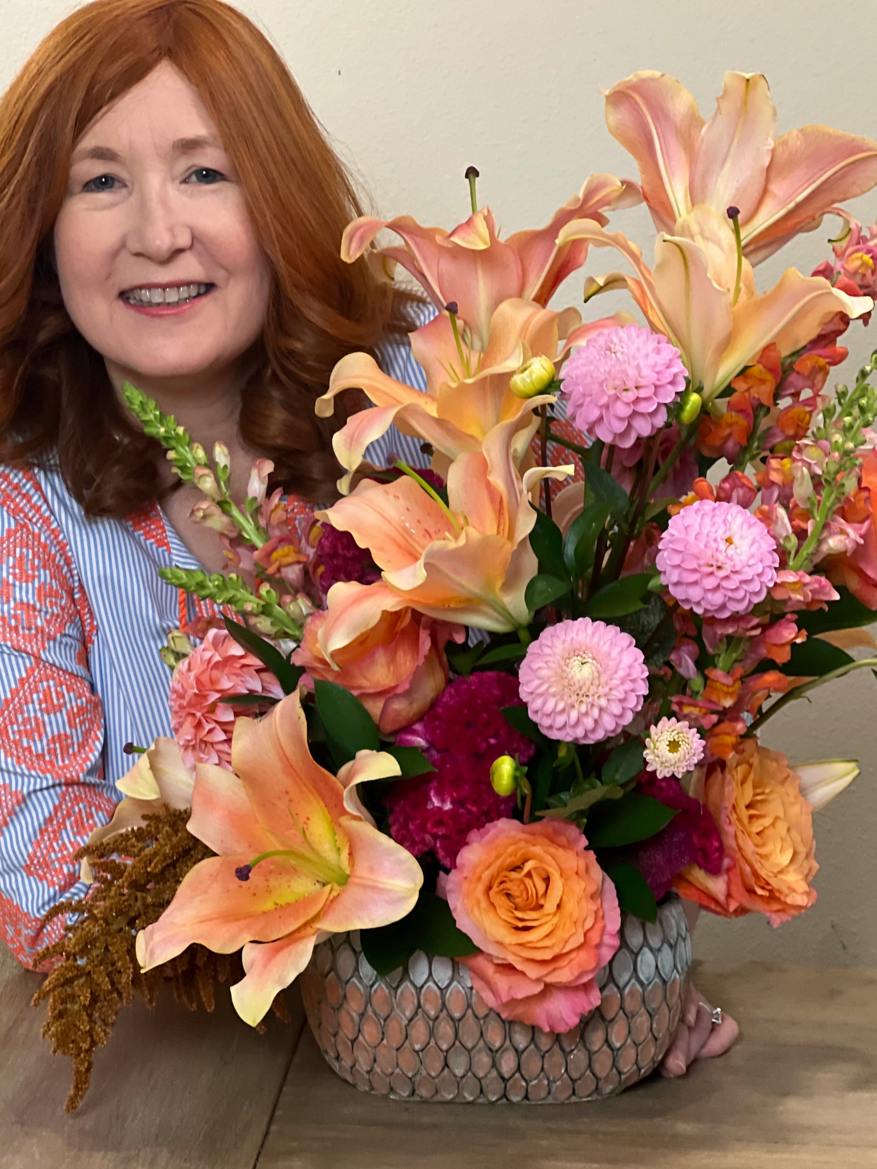 Los Angeles florist, Janice Pearson, holding an arrangement featuring peach lilies, pink dahlias, magenta celosia, and Free Spirit roses.