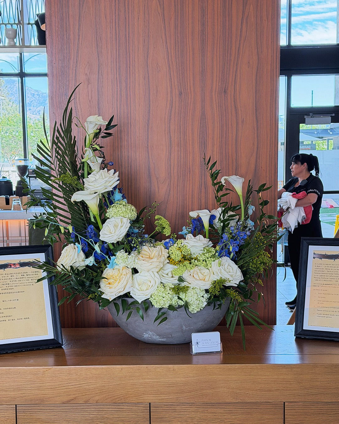 Hospitality floral arrangement on a wooden table in the bar area featuring calla lilies, roses, and palms.