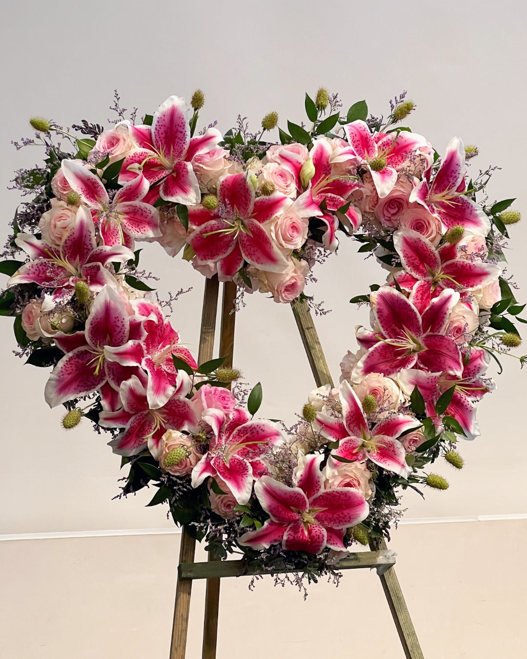 Floral wreath with roses and stargazer lilies on a stand against a light background.