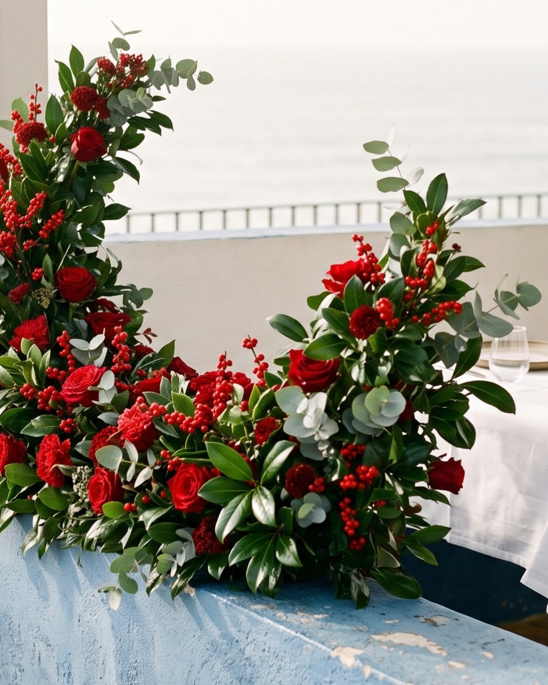 Red roses, berries and eucalyptus holiday arrangement at outdoor restaurant entrance.