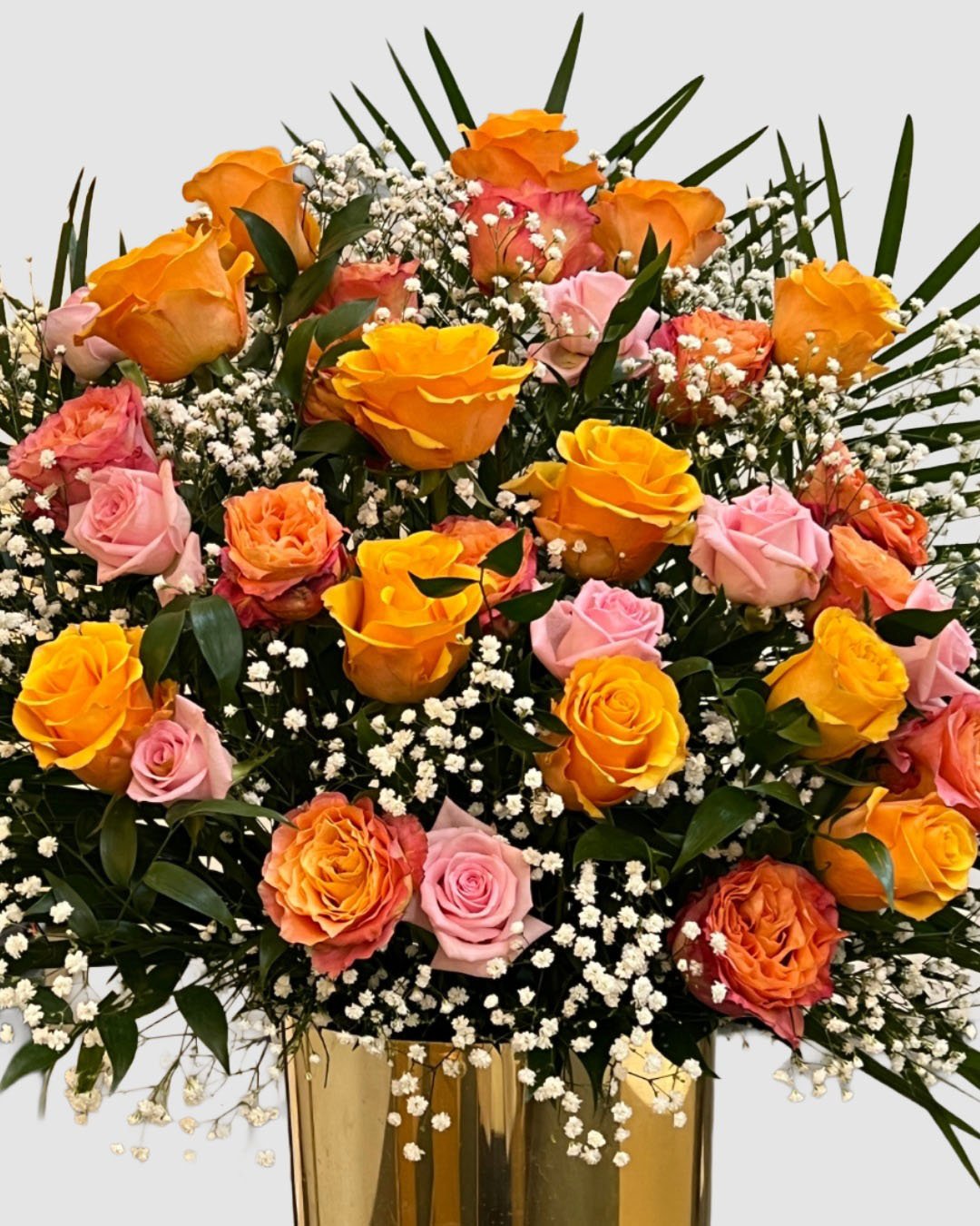 Lush peach, pink, and golden rose arrangement with baby’s breath in a gold vessel.