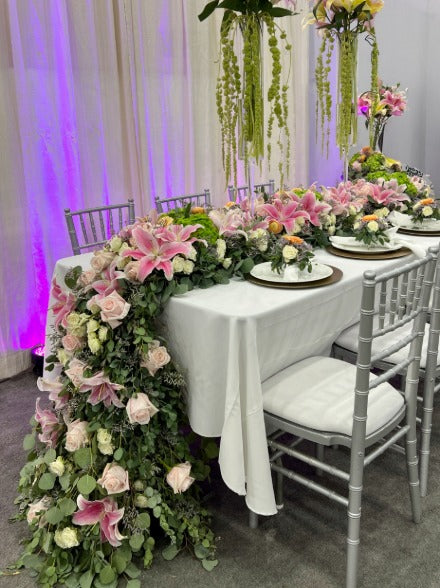 Decorated table with floral arrangements and chairs in a room with purple lighting.