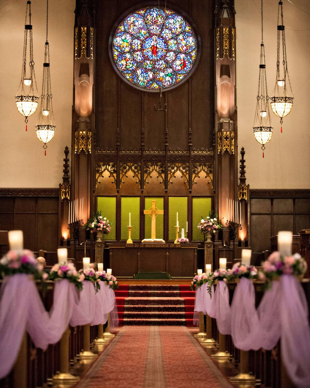 Church wedding ceremony center aisle draped in lavender fabric and connected to pedestal floral arrangements.
