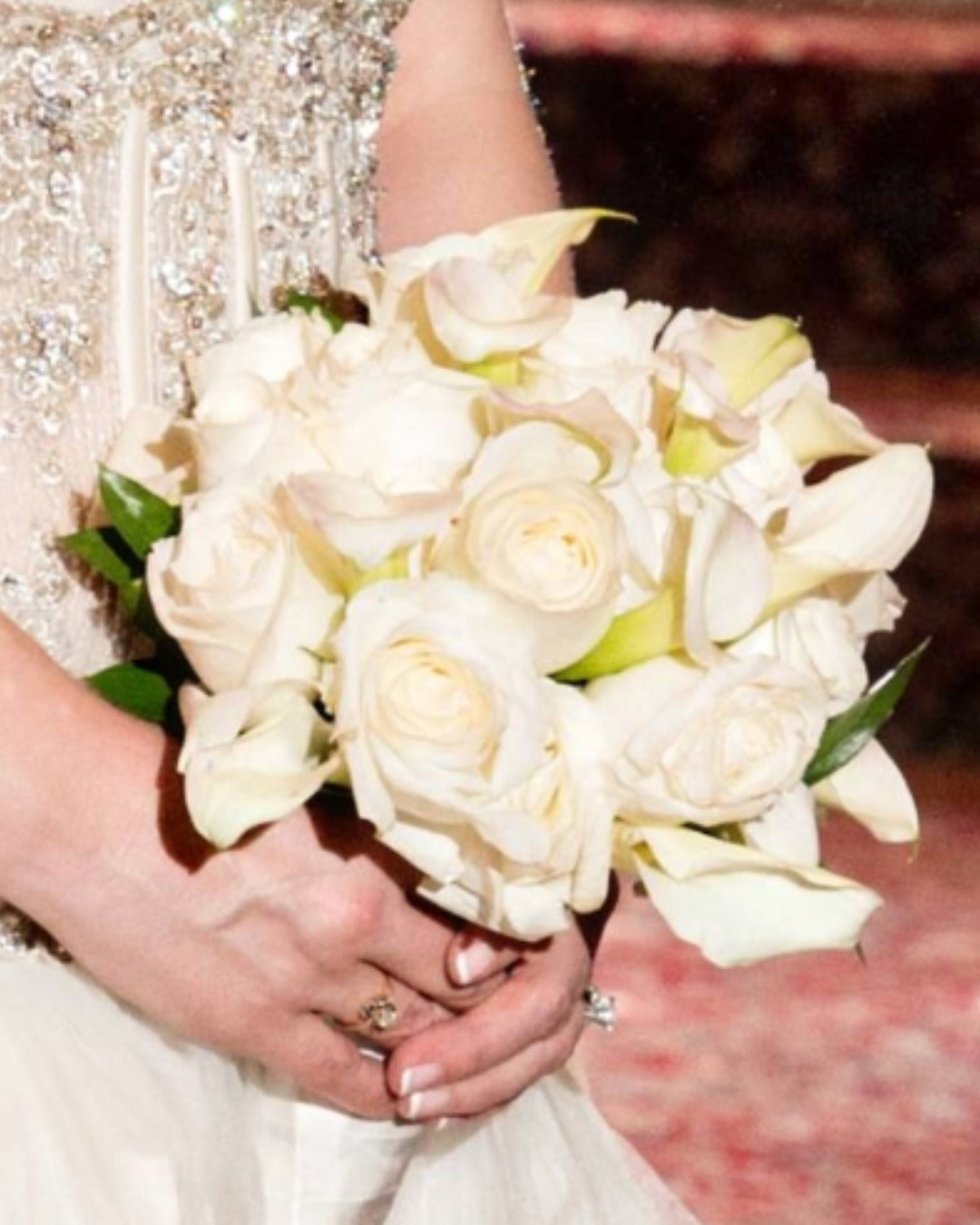 Bridal bouquet of white roses and calla lilies held against a white wedding dress.