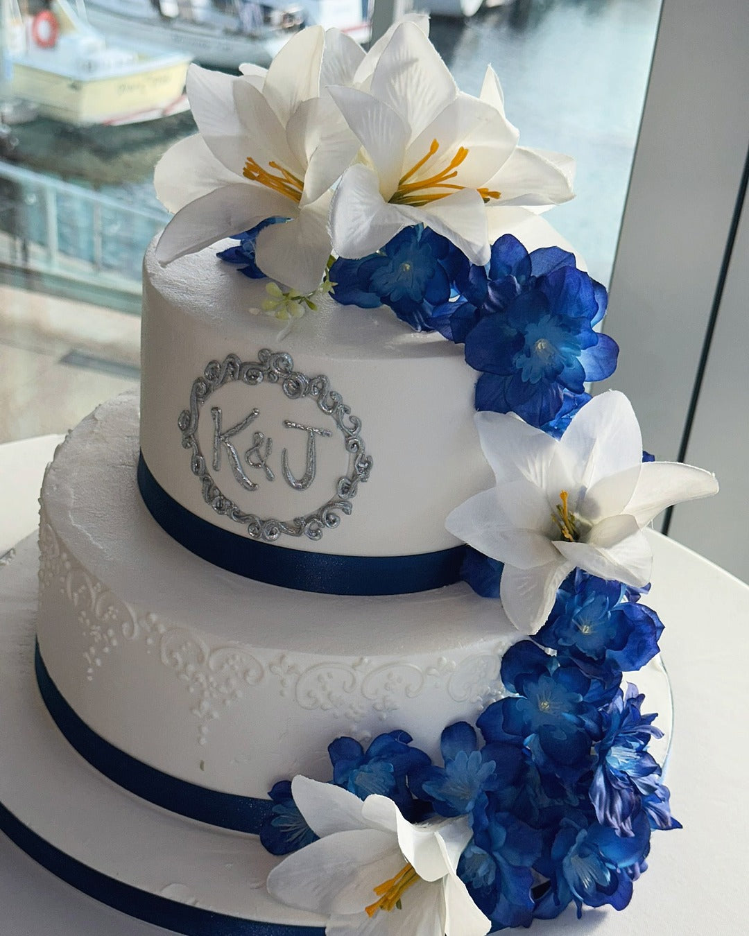 Two-tier wedding cake with artificial delphinium petals and white Easter lilies. 