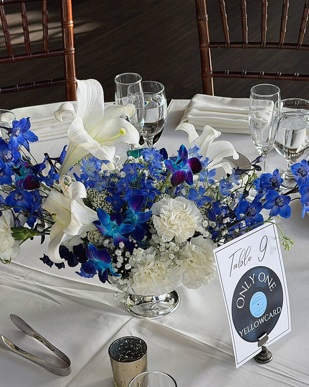 Reception table centerpiece with white carnations and Easter lilies, electric blue delphinium, and indigo dendrobium orchids.