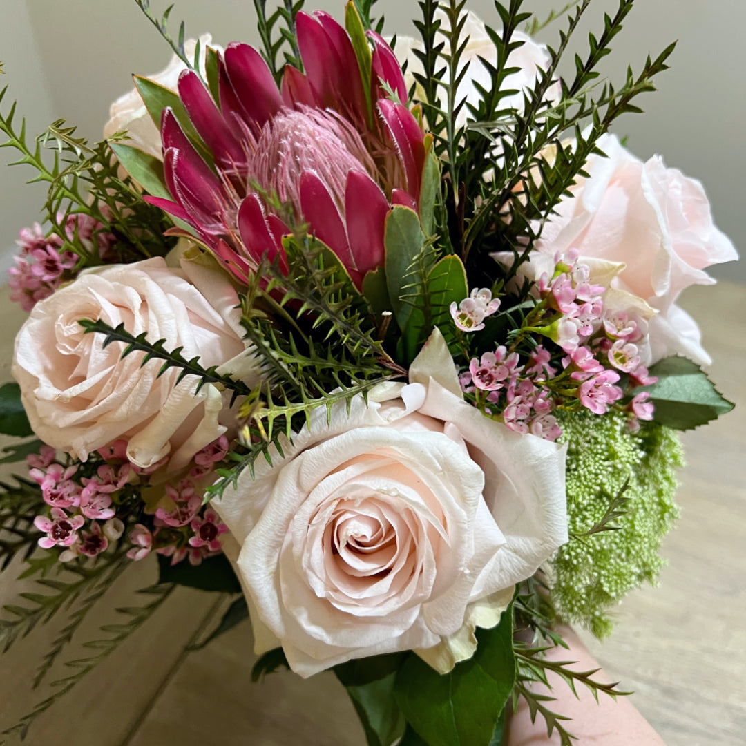 Bridal bouquet with protea, pink roses, green mist, grevillea, and leptospermum in a modern, textural design