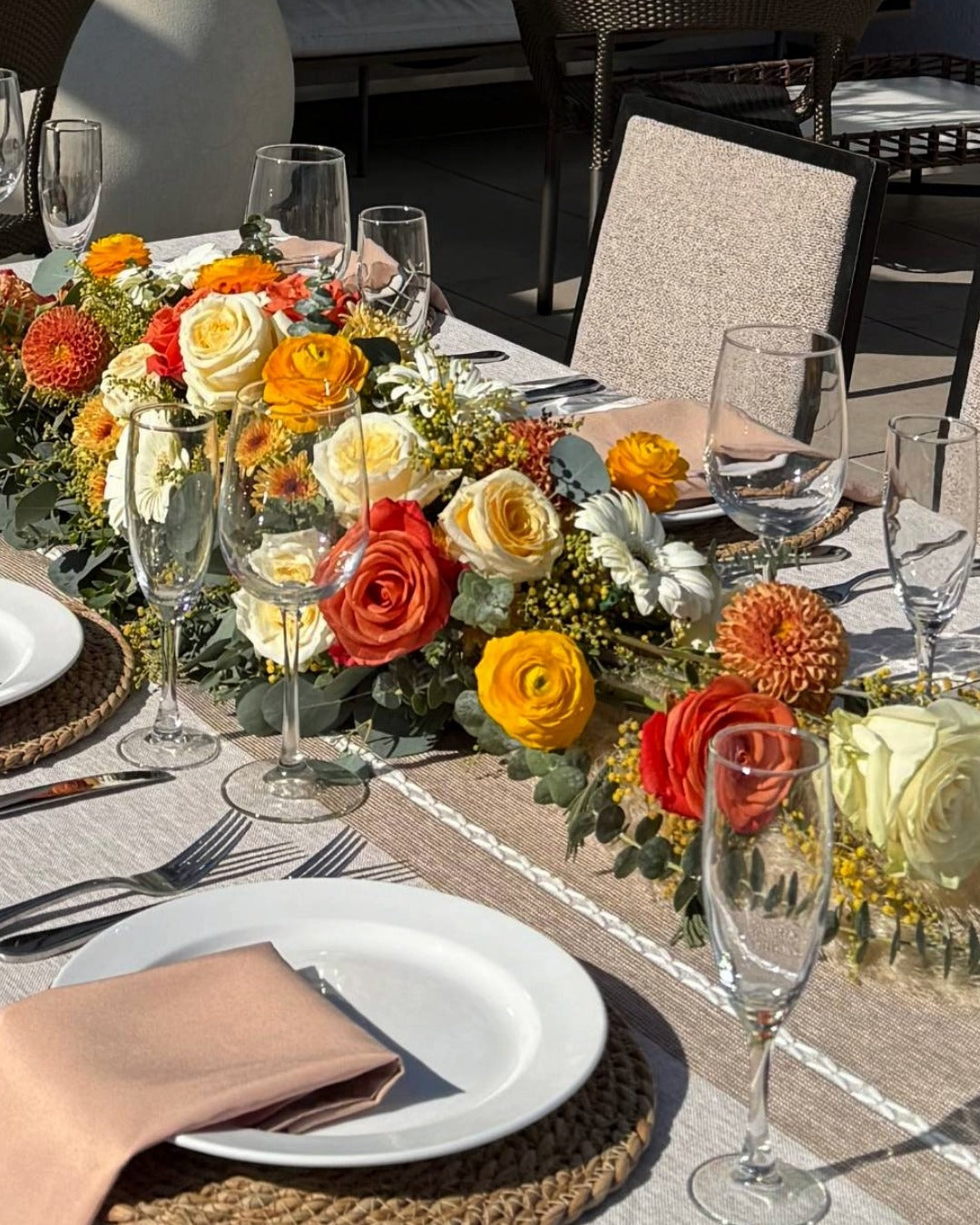 Decorative table setting with flowers, plates, and glasses on a patio.