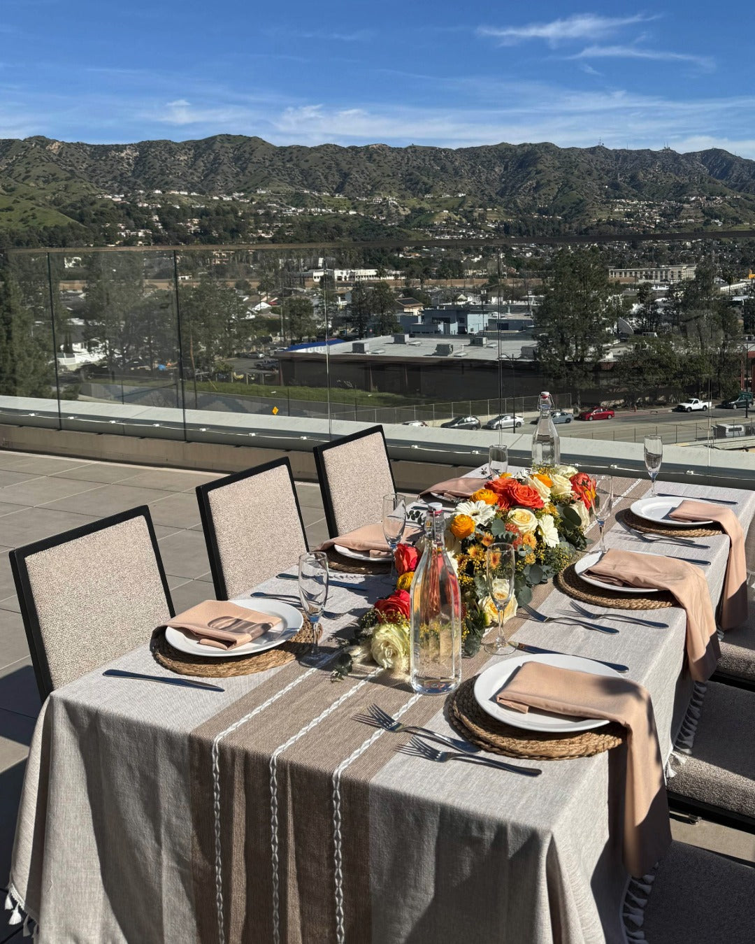 Outdoor dining table set with flowers and plates, overlooking a scenic landscape.