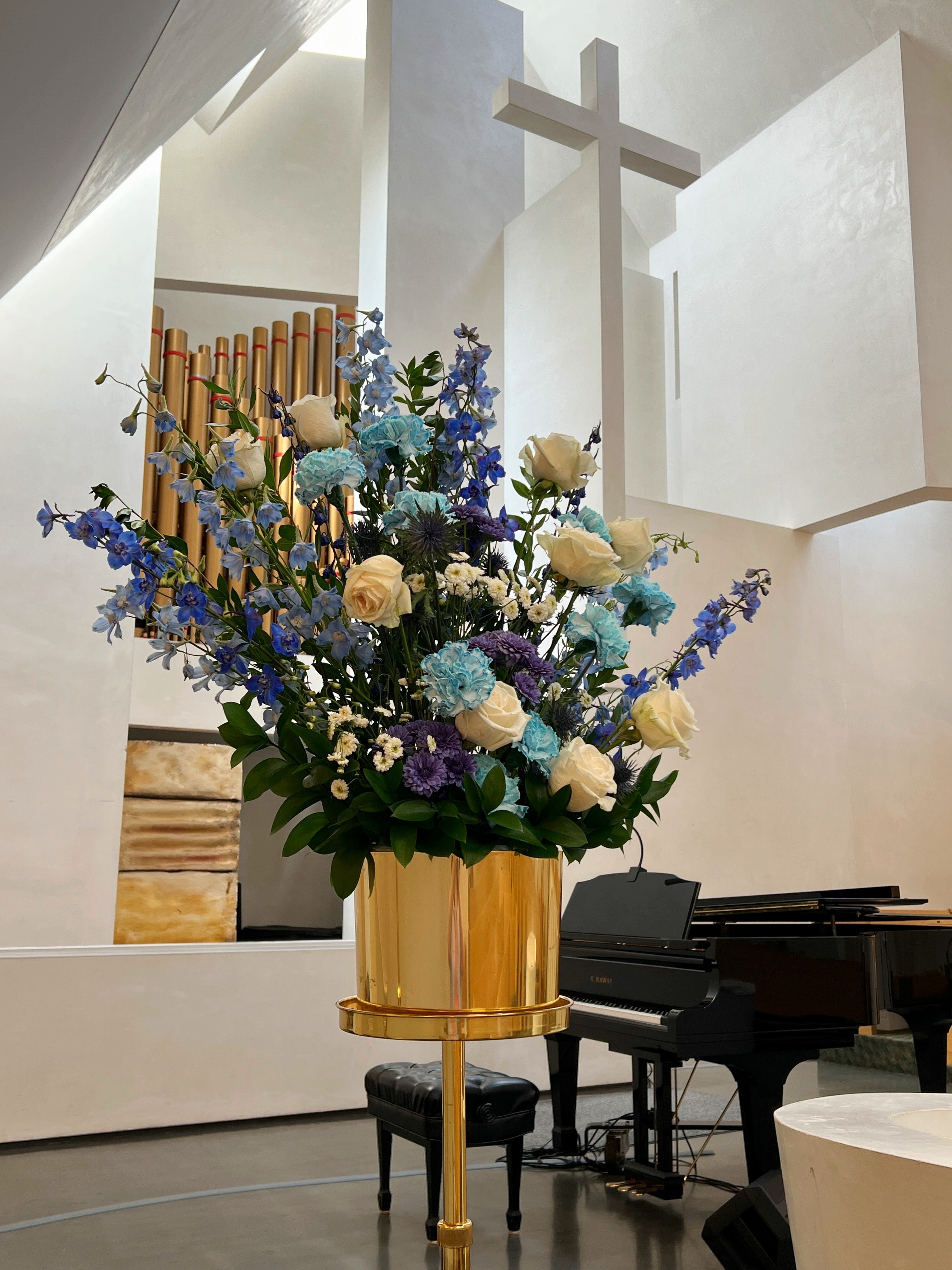 Blue celebration of life pedestal floral arrangement in a church setting with a cross and organ in the background.