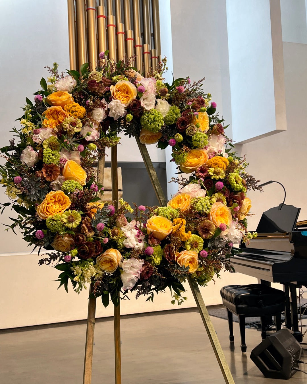 Floral wreath featuring yellow garden roses, green zinnias, white and purple lisianthus, and purple clover for celebration of life.