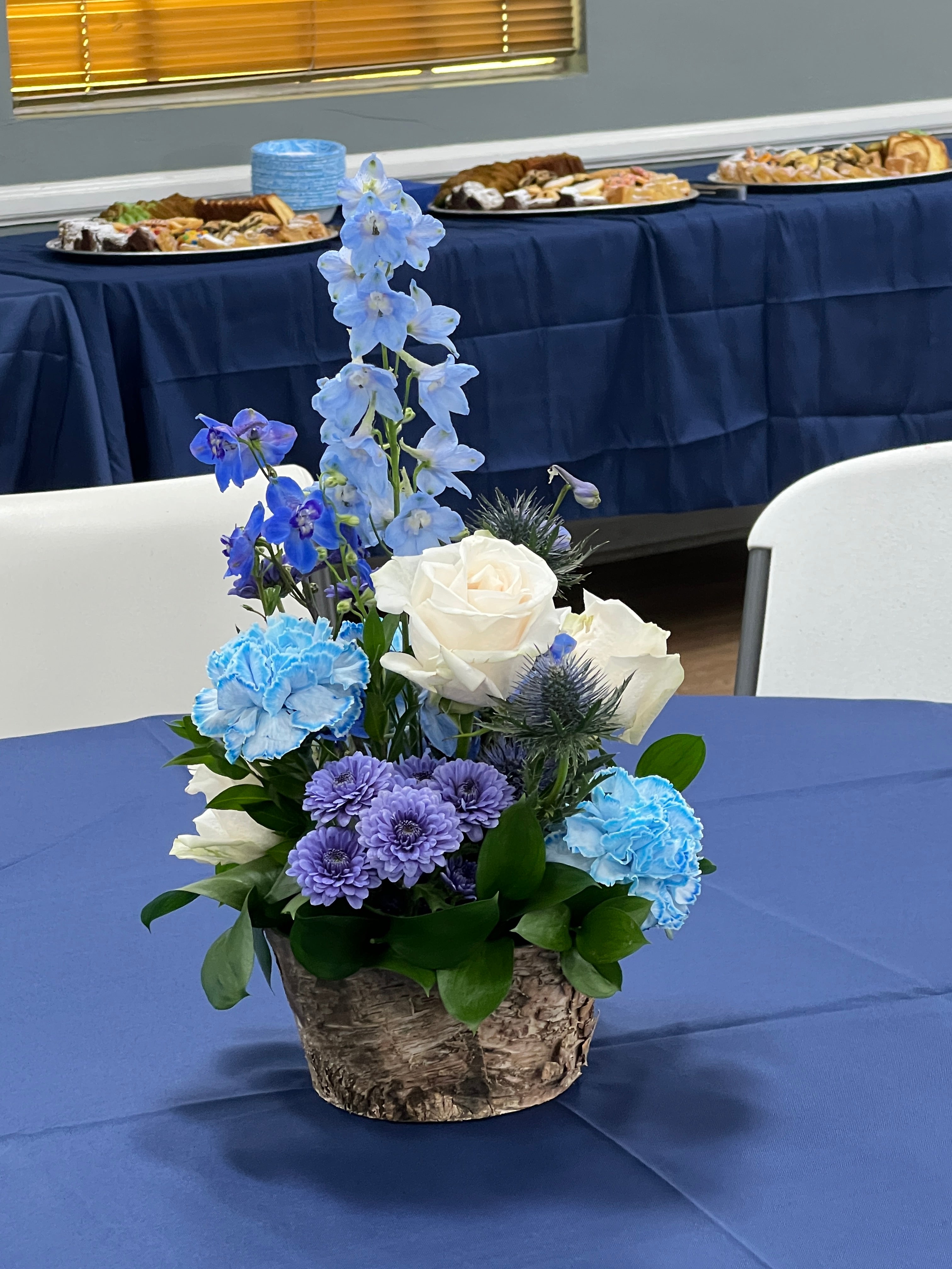 Blue and white floral arrangement for celebration of life reception featuring carnations, roses, delphinium, and button pompon mums.