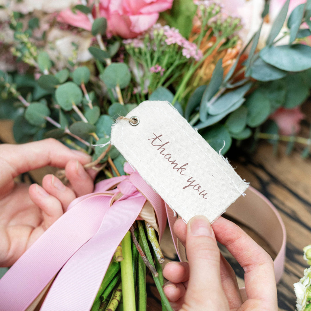 A close-up of a thank you note attached to a blurred bouquet in the background.