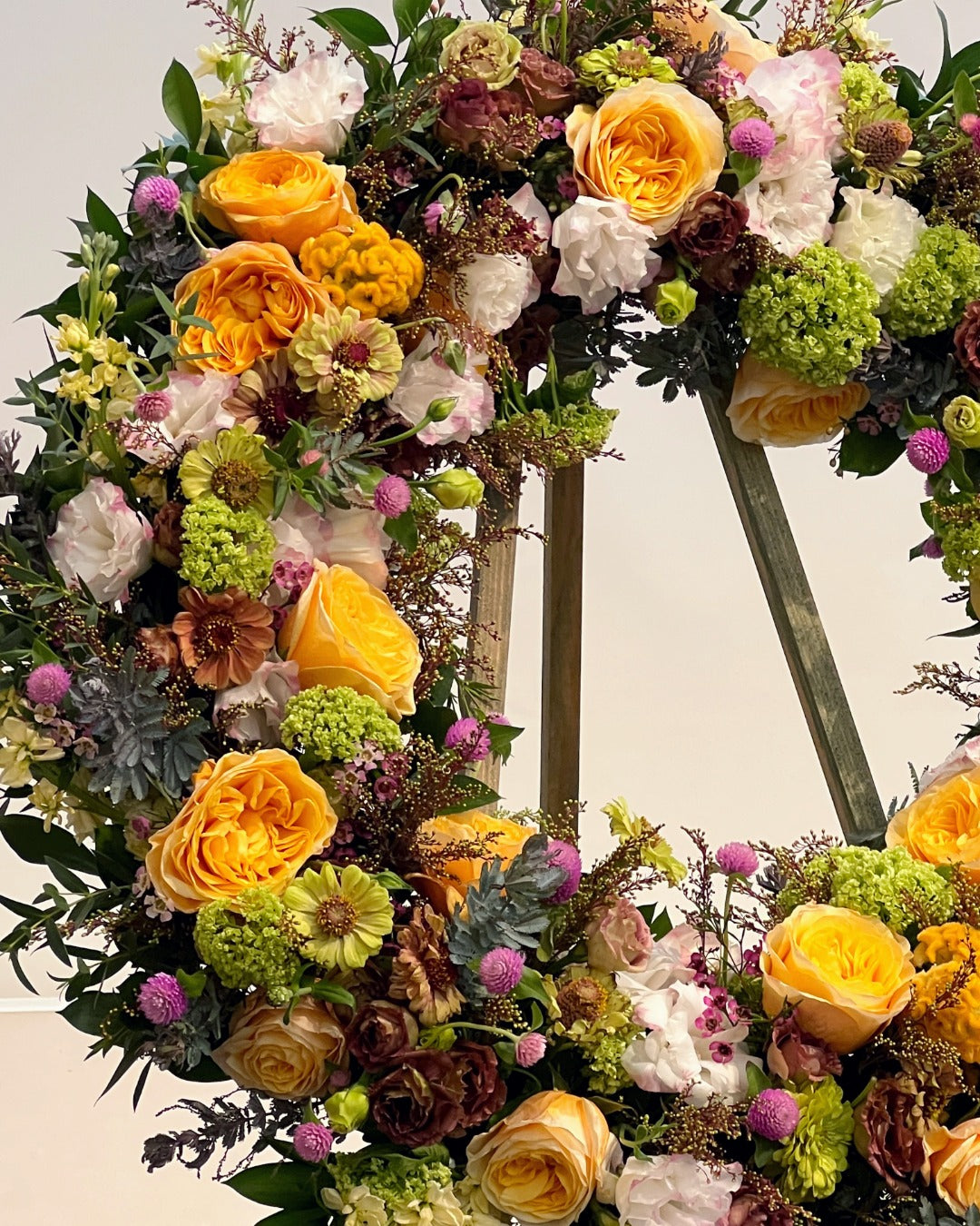 Closeup of wreath tribute with yellow garden roses, white and lavender lisianthus, green zinnias, and purple clover for celebration of life service.