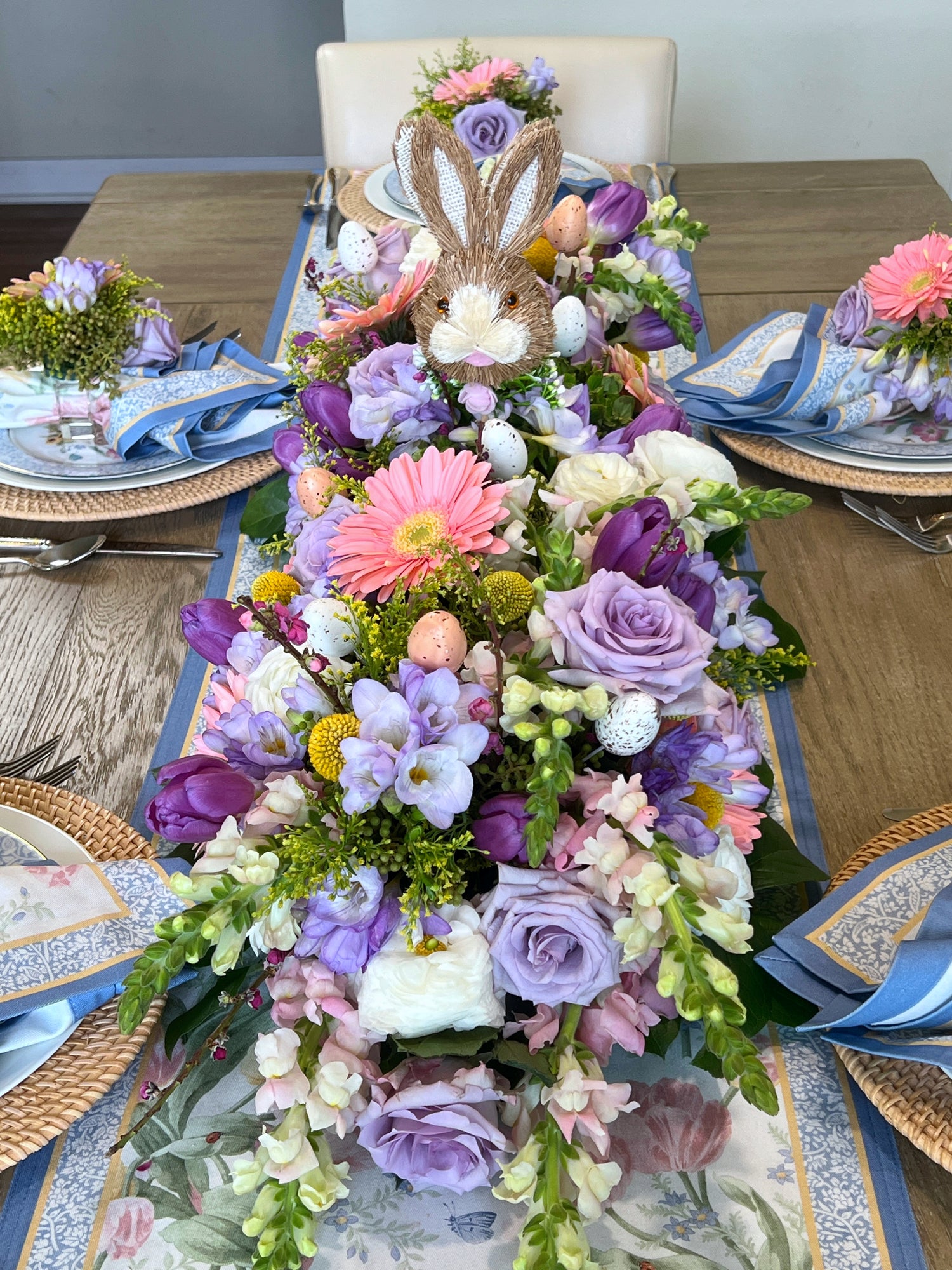 Easter table centerpiece featuring a bunny head, Easter eggs, Gerber daisies, freesias, ranunculus, tulips, and Billy balls