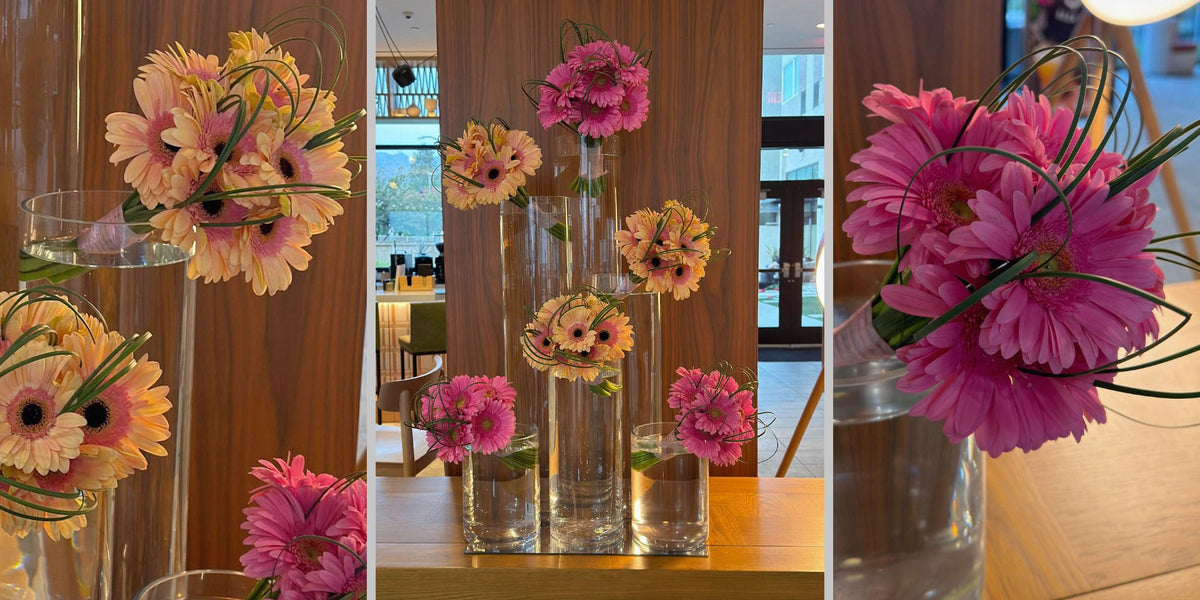 Hotel lobby floral installation with six hot pink and peach gerbera daisy bouquets forming interlocking triangles in glass cylinder vases.