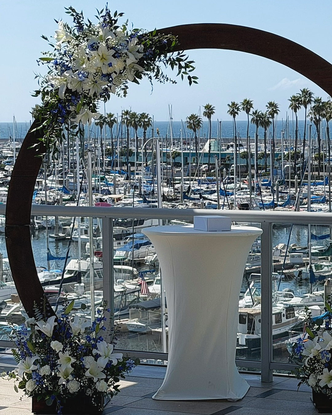 Wedding arch at waterfront wedding featuring white lilies, electric blue delphinium, white carnations, and greens.