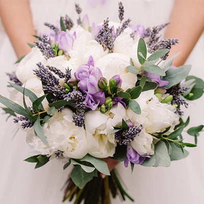 Luxe wedding bouquet featuring white peonies, lavender, and eucalyptus held by bride.