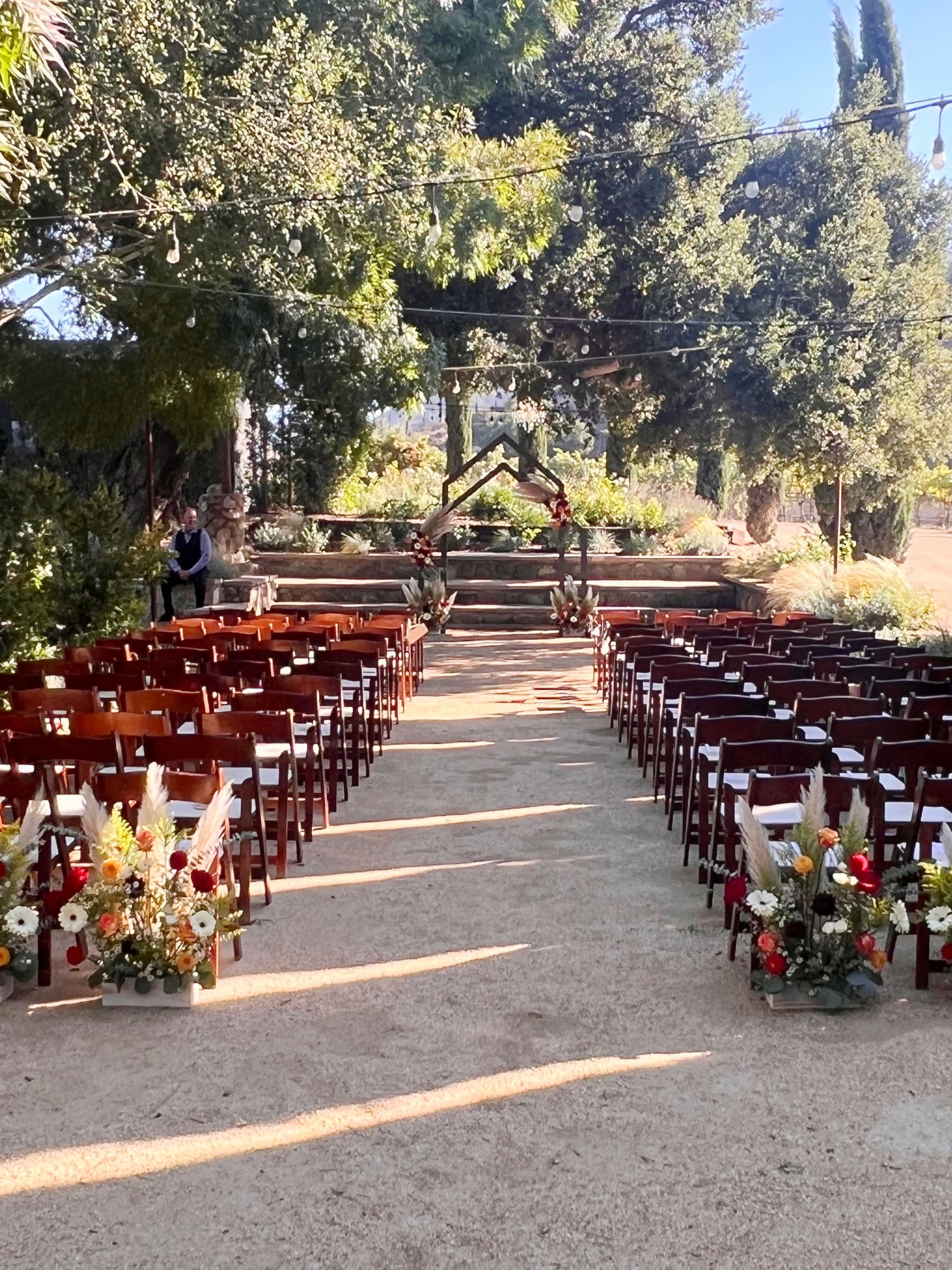 Vineyard wedding aisle featuring floral arrangements in back of the last row of chairs and arch.