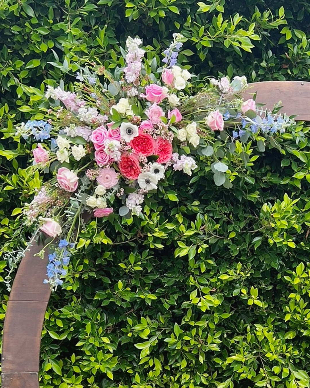 Close-up of top arch installation featuring delphinium, roses, anemones, stock, wax flower, eucalyptus and Italian Ruscus.