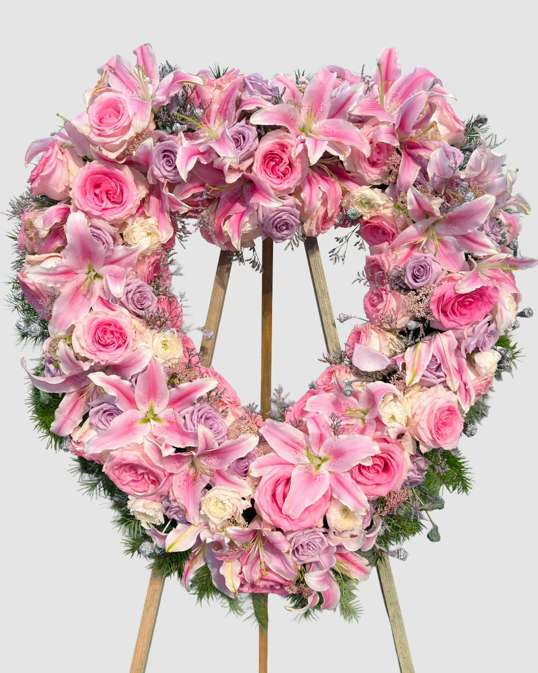 Heart-shaped floral arrangement with pink lilies, white and pink roses, and pine greens for a celebration of life service.
