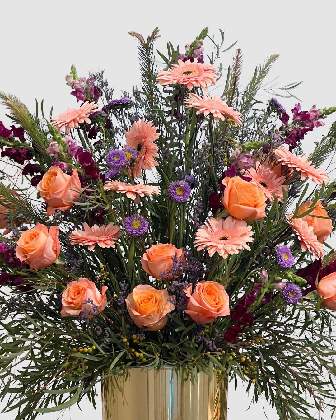 Peach and plum garden-style floral arrangement with roses, Gerbera daisies, snapdragons, and aster. 