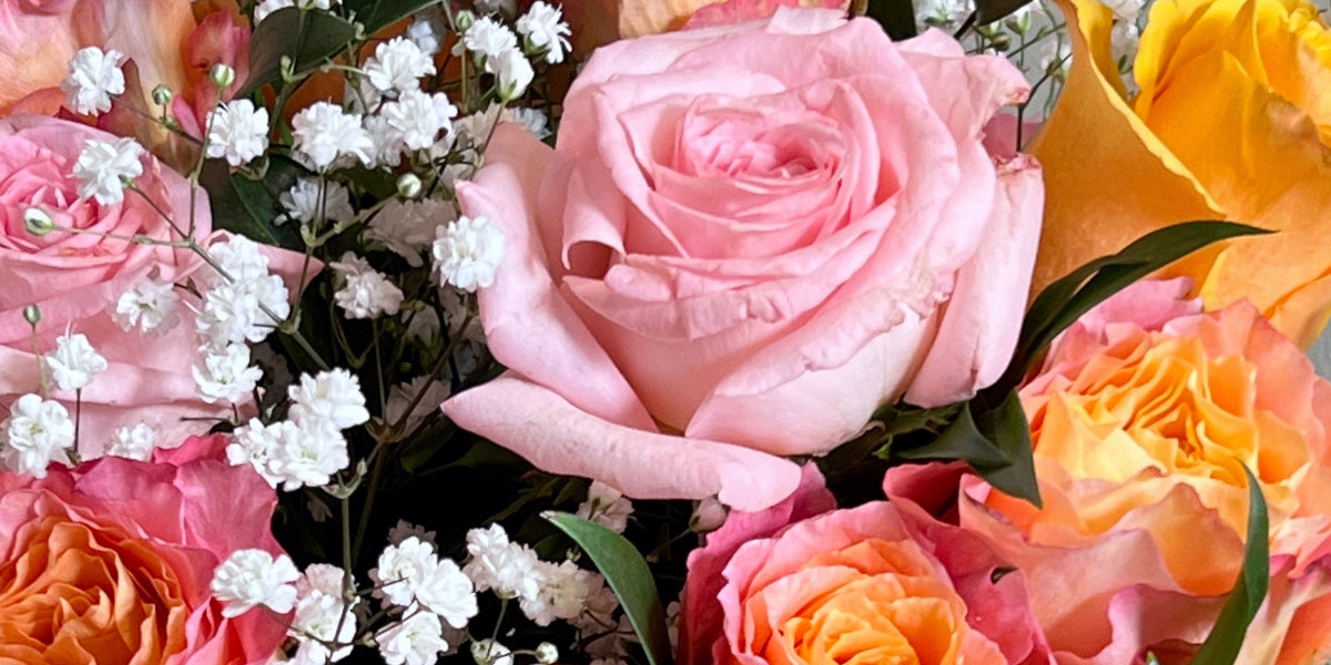 Close-up of a romantic floral arrangement with roses, baby’s breath, and Italian ruscus, designed for a website image banner