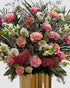 Peach and blush garden-style arrangement with roses, celosia, zinnias, scabiosa, and snapdragons in a gold vase.