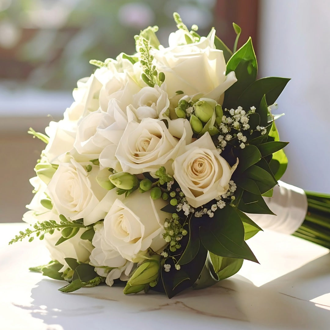 A bridal bouquet featuring white roses, green foliage, and small white baby's breath.