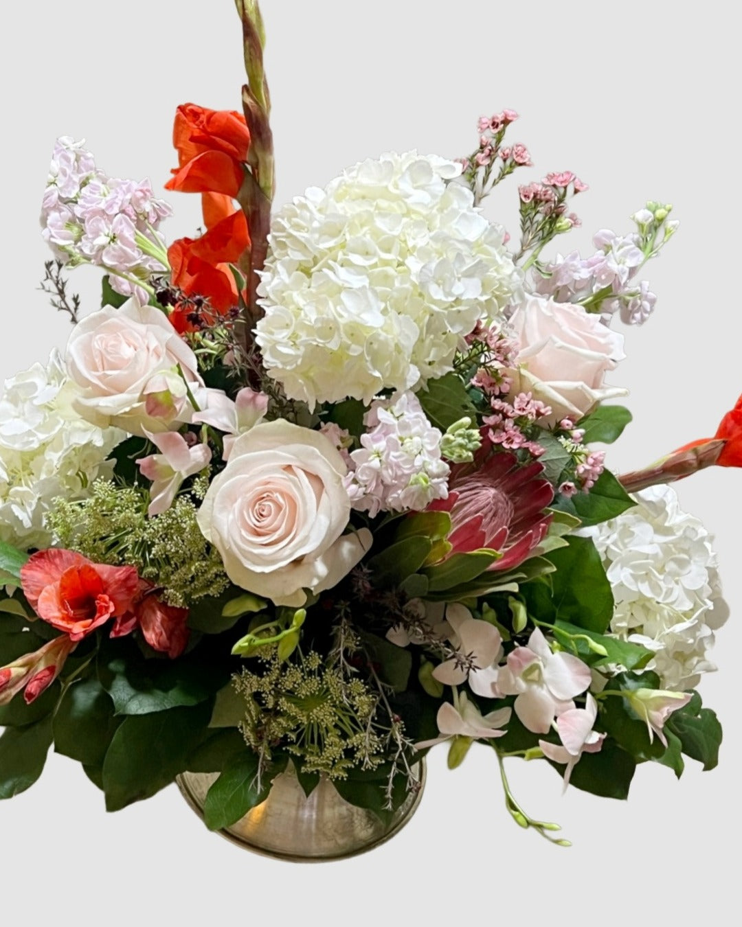 Soft pastel arrangement with hydrangeas, roses, and orchids in blush and cream tones for gifting.