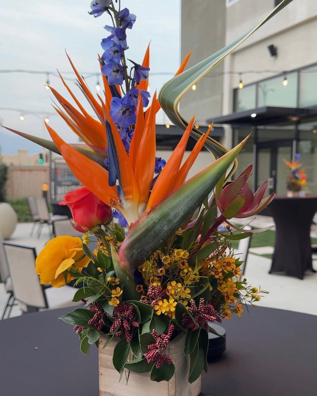 Modern tropical floral arrangement with birds of paradise, blue delphinium, and sculptural greenery for a corporate networking event.