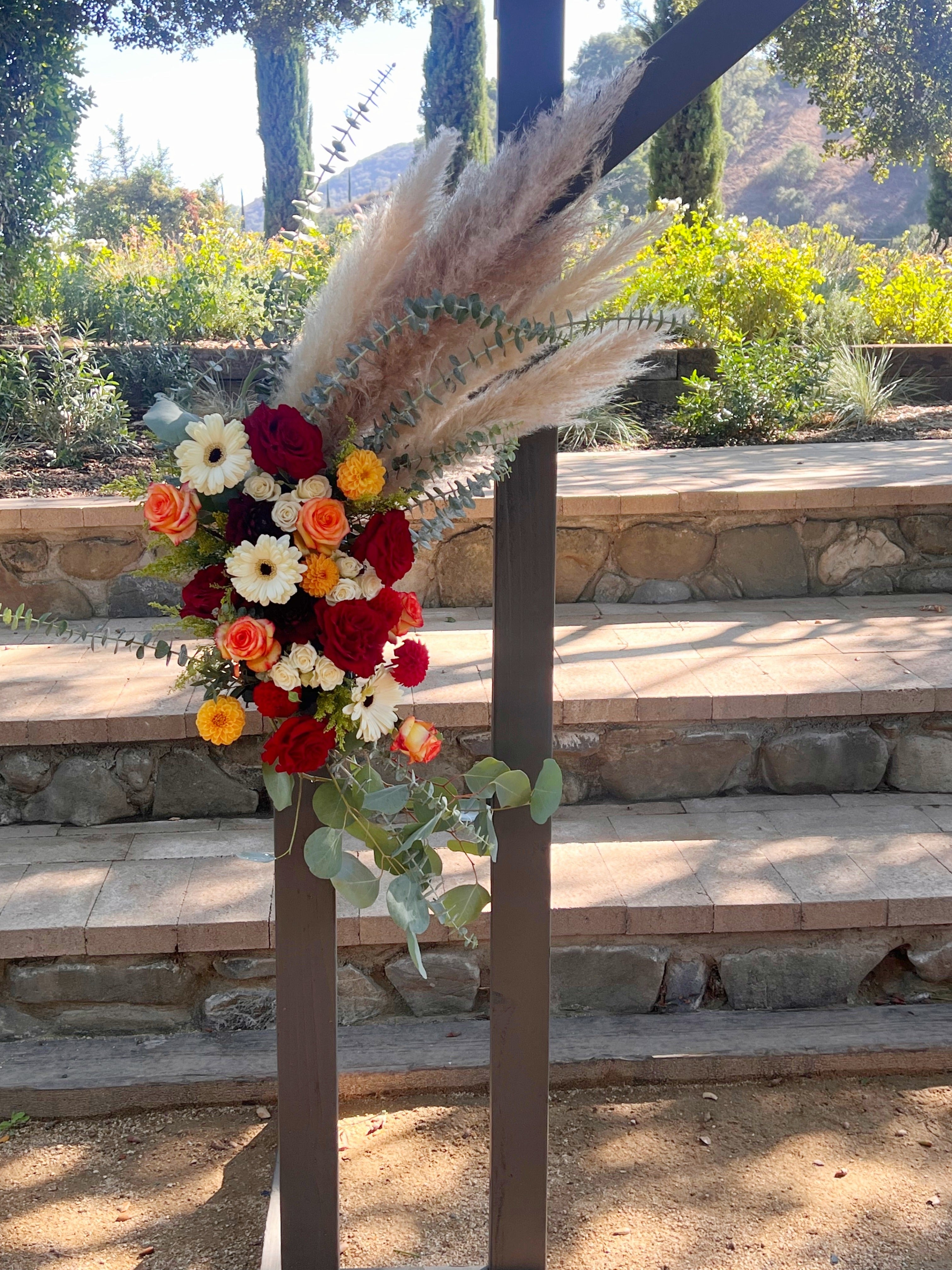 Close-up of the arch's left attached floral installation featuring pampas grass, dahlias, roses, and gerbera daisies.