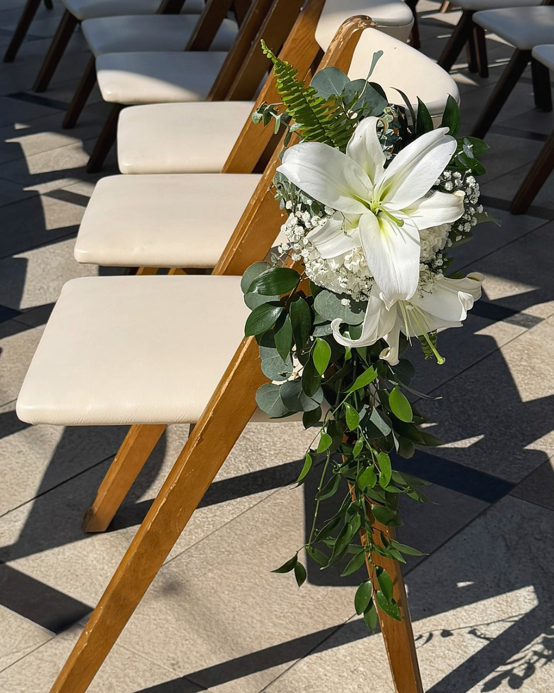 Wedding ceremony aisle arrangement attached to chair featuring lilies, carnations, baby's breath and greens.
